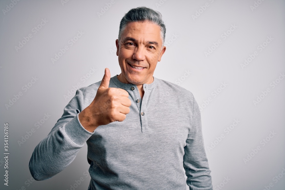 Middle age handsome grey-haired man wearing casual t-shirt over white background doing happy thumbs up gesture with hand. Approving expression looking at the camera showing success.