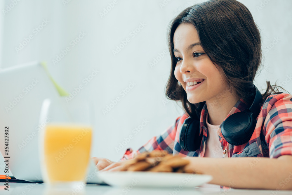 Gladsome girl with orange juice and cookies in front of gadget Gladsome girl with orange juice and cookies in front of gadget
