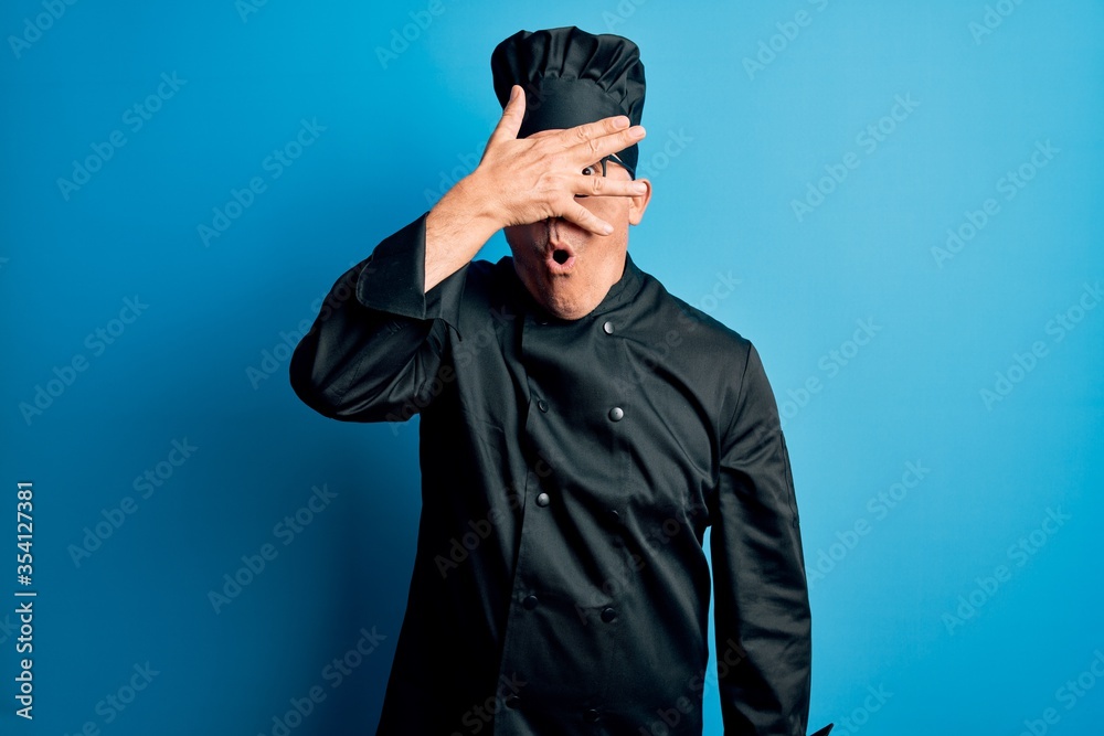 Middle age handsome grey-haired chef man wearing cooker uniform and hat peeking in shock covering face and eyes with hand, looking through fingers with embarrassed expression. Middle age handsome grey-haired chef man wearing cooker uniform and hat peeking in shock covering face and eyes with hand, looking through fingers with embarrassed expression.