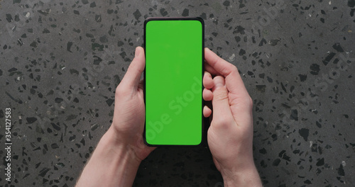 Top view man hand show smartphone with green screen on concrete background