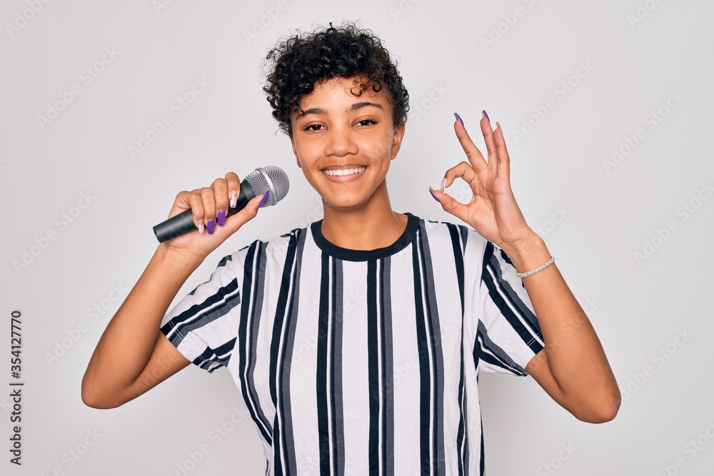 Beautiful african american afro singer woman singing using microphone over white background doing ok sign with fingers, excellent symbol Beautiful african american afro singer woman singing using microphone over white background doing ok sign with fingers, excellent symbol