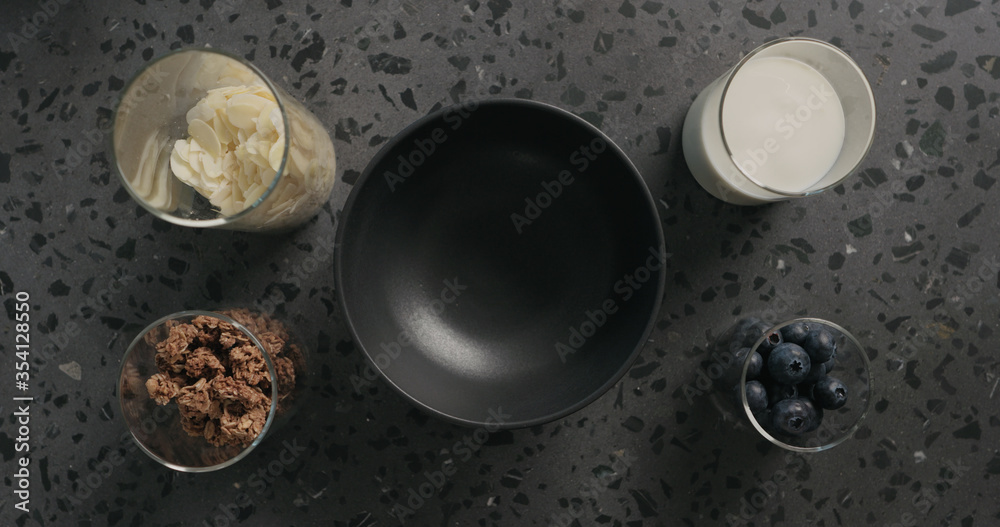 breakfast with chocolate granola, almond flakes and blueberry in black bowl on terrazzo surface breakfast with chocolate granola, almond flakes and blueberry in black bowl on terrazzo surface