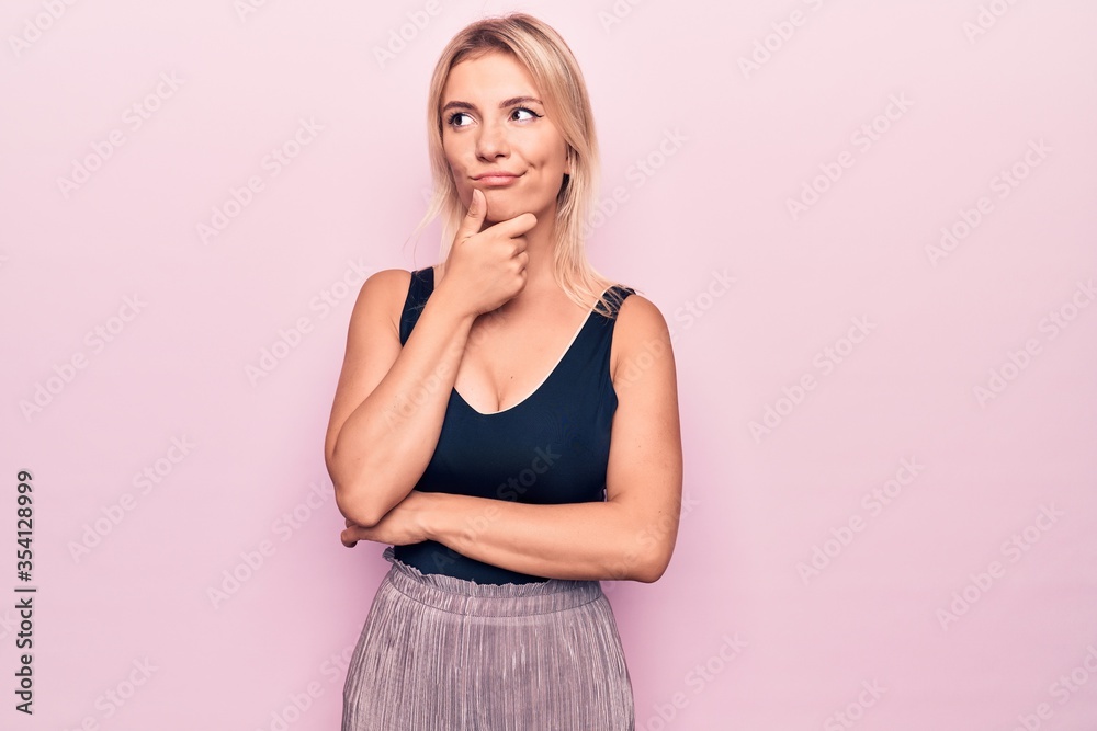Young beautiful blonde woman wearing casual black t-shirt standing over pink background thinking concentrated about doubt with finger on chin and looking up wondering Young beautiful blonde woman wearing casual black t-shirt standing over pink background thinking concentrated about doubt with finger on chin and looking up wondering