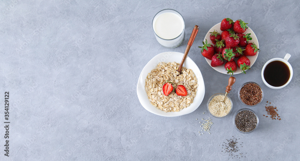Ingredients for healthy breakfast concept banner. Bowl of oatmeal porridge, strawberries, milk and seeds on stone background with copy space