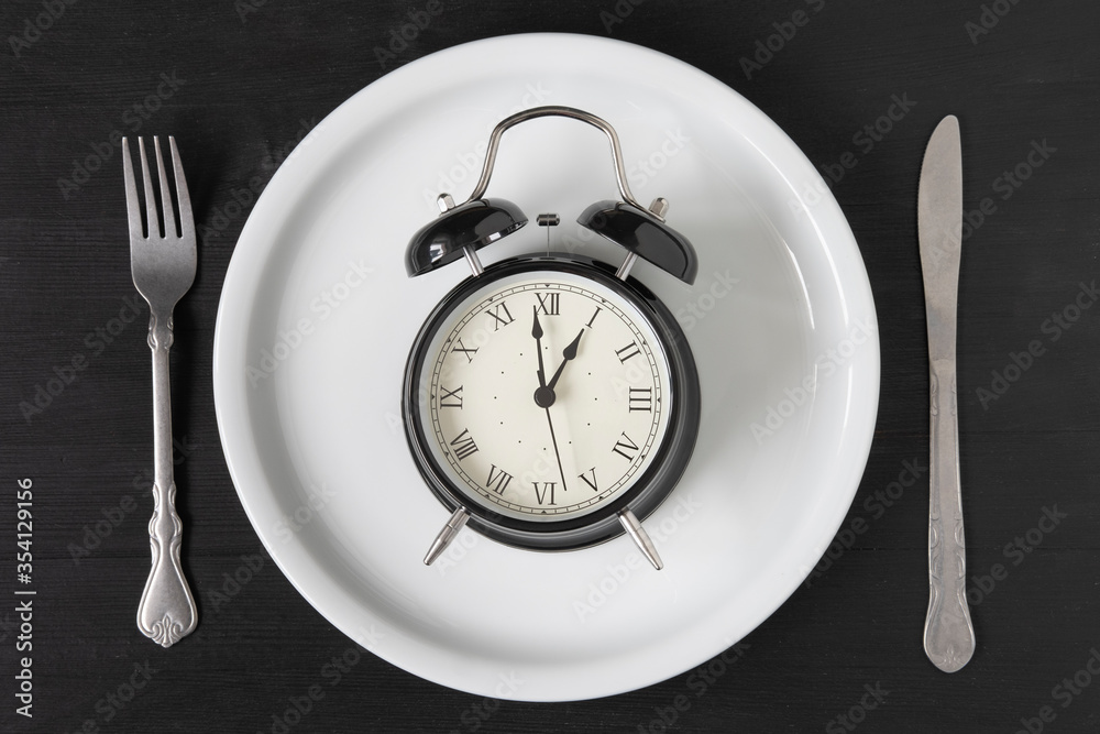 Alarm clock on a white plate with a knife and fork Alarm clock on a white plate with a knife and fork