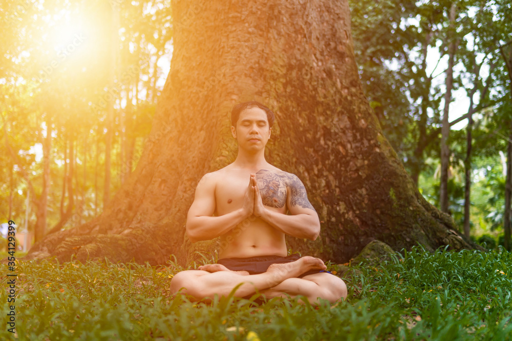 Young asian man are wiping sweat and doing yoga exercises in park. Under big tree. Young asian man are wiping sweat and doing yoga exercises in park. Under big tree.