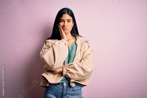 Young beautiful hispanic fashion woman wearing winter jacket and sweater over pink background thinking looking tired and bored with depression problems with crossed arms.