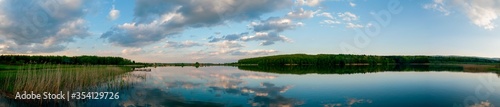 Panoramic landscape from the lake shore with colorful clouds in the spring sun.