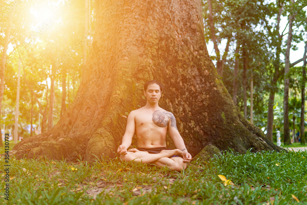Young asian man are wiping sweat and doing yoga exercises in park. Under big tree. Young asian man are wiping sweat and doing yoga exercises in park. Under big tree.