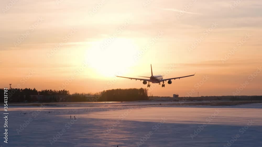 Silhouette of a passenger plane that lands at the airport at sunset in winter