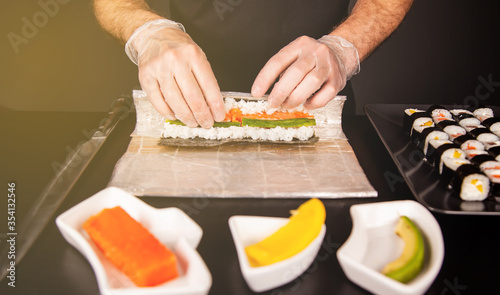 Cook hands making Japanese sushi roll. Japanese chef at work preparing delicious sushi roll with eel and avocado