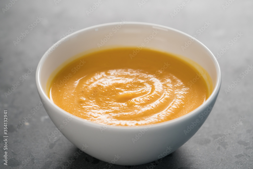 Pumpkin spicy soup puree in white bowl on concrete background Pumpkin spicy soup puree in white bowl on concrete background