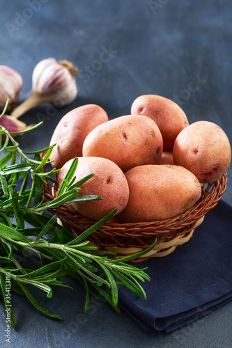 Red raw potatoes with fresh rosemary and garlic on a blue background. Still life