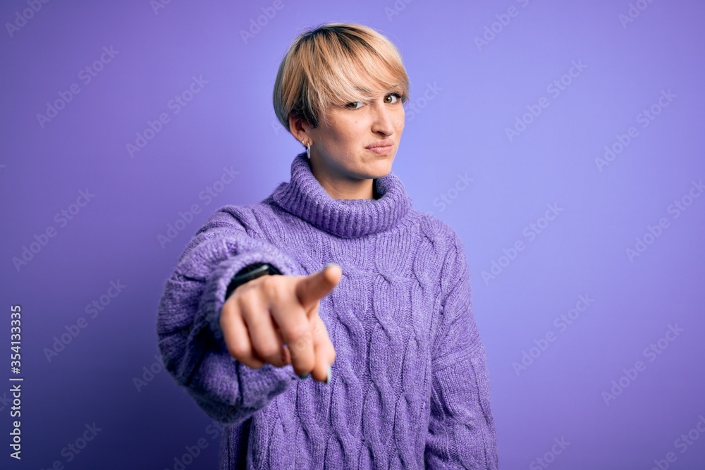 Young blonde woman with short hair wearing winter turtleneck sweater over purple background pointing displeased and frustrated to the camera, angry and furious with you Young blonde woman with short hair wearing winter turtleneck sweater over purple background pointing displeased and frustrated to the camera, angry and furious with you