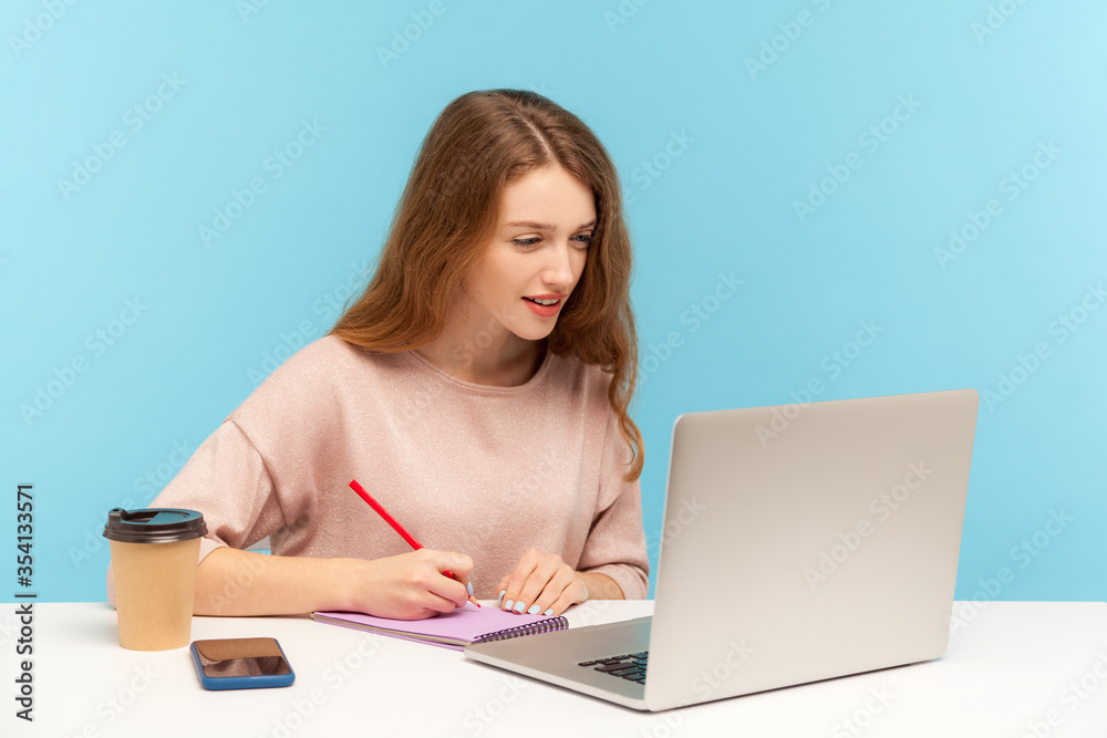 Woman journalist working on laptop and making notes on paper. Student studying, writing in notebook while listening online school, internet course. indoor studio shot isolated on blue background Woman journalist working on laptop and making notes on paper. Student studying, writing in notebook while listening online school, internet course. indoor studio shot isolated on blue background