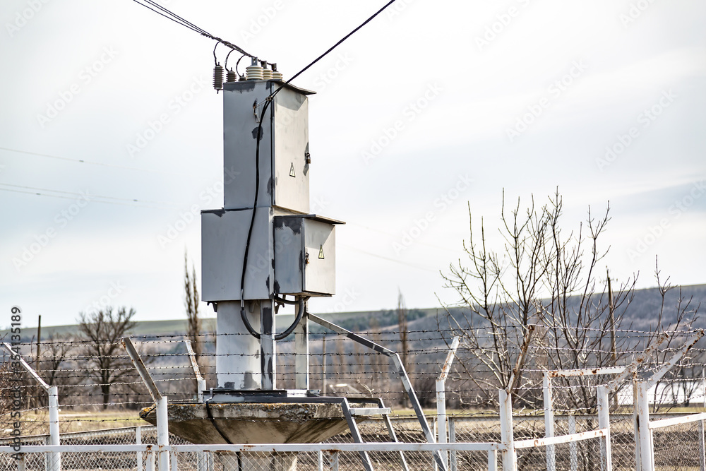 A small complete transformer substation behind the barbed wire fence is located in the field. Horizontal orientation.