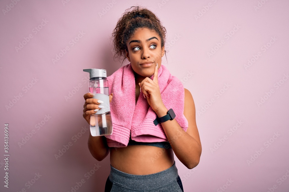 Young african american sporty girl doing sport wearing towel drinking bottle of water serious face thinking about question, very confused idea Young african american sporty girl doing sport wearing towel drinking bottle of water serious face thinking about question, very confused idea