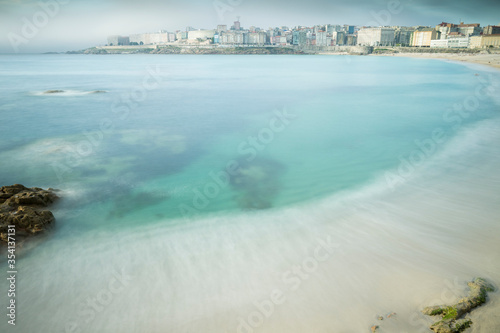 Playa del orzán de A Coruña durante una tarde de verano y cubierta por la niebla. Mar azul y rocas.