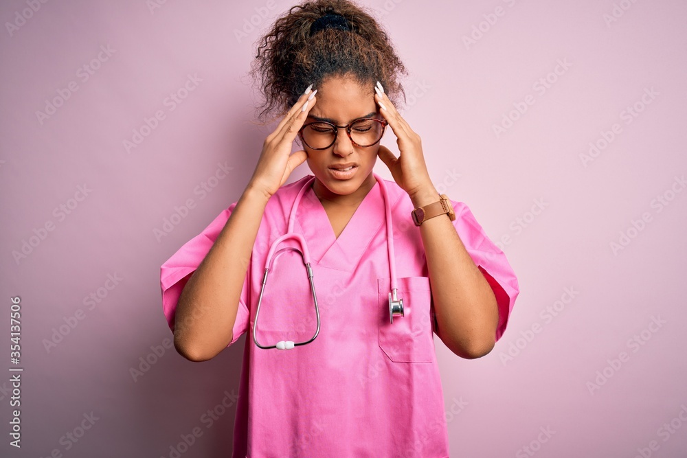 African american nurse girl wearing medical uniform and stethoscope over pink background with hand on head for pain in head because stress. Suffering migraine. African american nurse girl wearing medical uniform and stethoscope over pink background with hand on head for pain in head because stress. Suffering migraine.