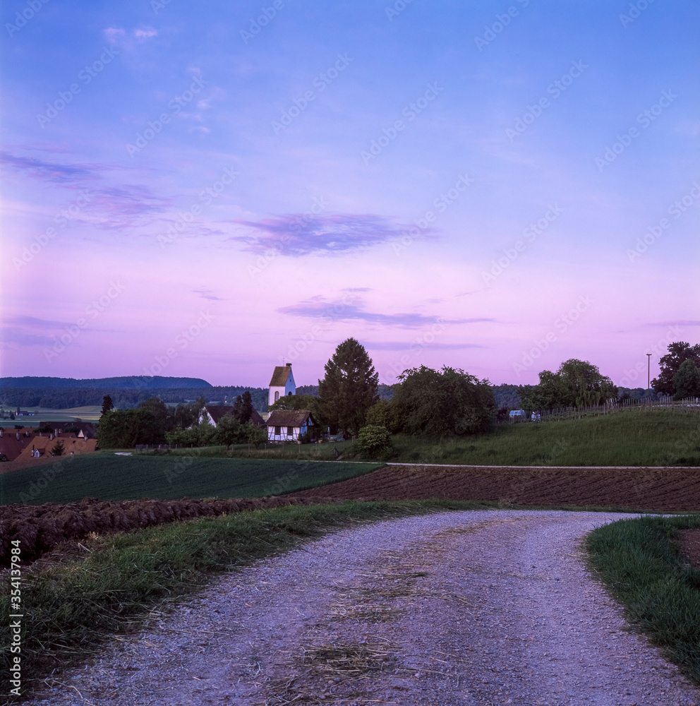 The gravel road leading to the church of Stadel in Switzerland at sunset, shot with analogue slide film technique The gravel road leading to the church of Stadel in Switzerland at sunset, shot with analogue slide film technique