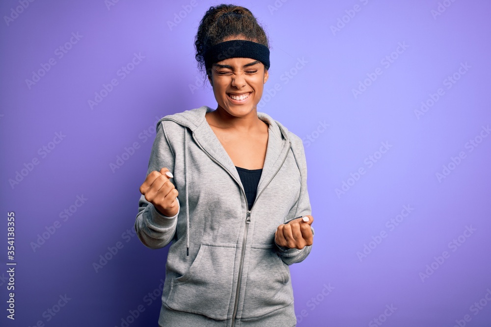 Young african american sportswoman doing sport wearing sportswear over purple background very happy and excited doing winner gesture with arms raised, smiling and screaming for success. Celebration Young african american sportswoman doing sport wearing sportswear over purple background very happy and excited doing winner gesture with arms raised, smiling and screaming for success. Celebration