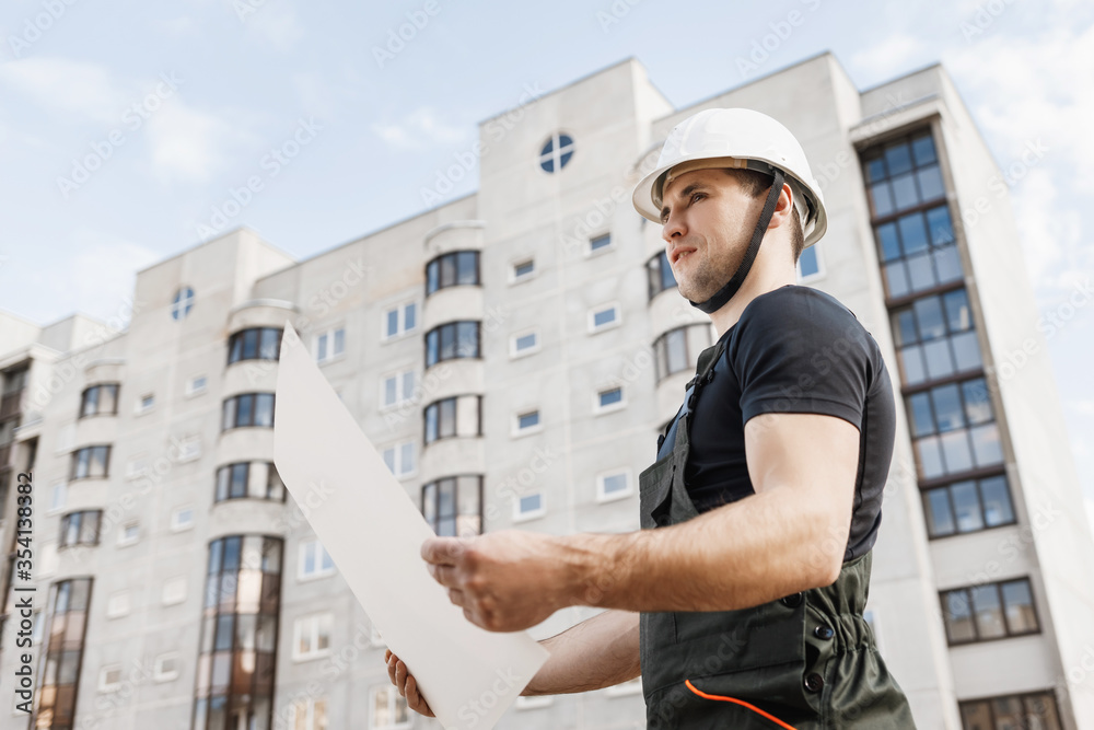 builder in helmet and with a drawing on the background of a house under construction builder in helmet and with a drawing on the background of a house under construction