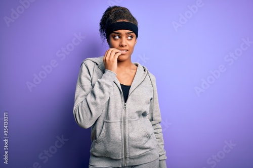 Young african american sportswoman doing sport wearing sportswear over purple background looking stressed and nervous with hands on mouth biting nails. Anxiety problem.