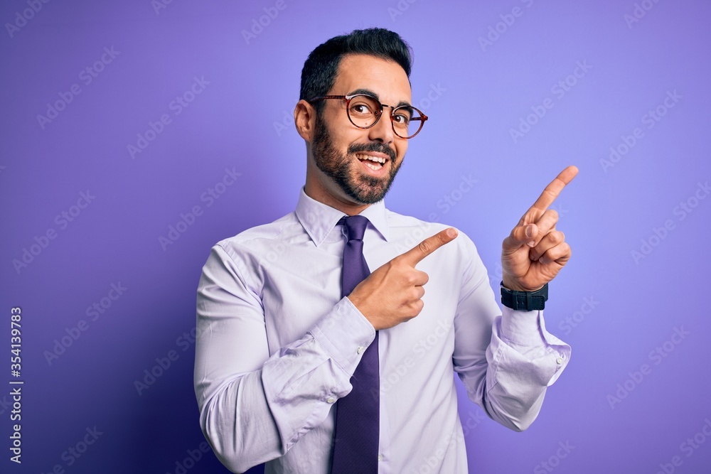 Handsome businessman with beard wearing casual tie and glasses over purple background smiling and looking at the camera pointing with two hands and fingers to the side. Handsome businessman with beard wearing casual tie and glasses over purple background smiling and looking at the camera pointing with two hands and fingers to the side.