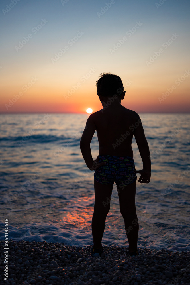 Little kid playing with the sun on the beach at sunset