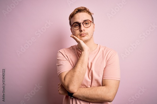 Young handsome redhead man wearing casual t-shirt standing over isolated pink background thinking looking tired and bored with depression problems with crossed arms. © Krakenimages.com