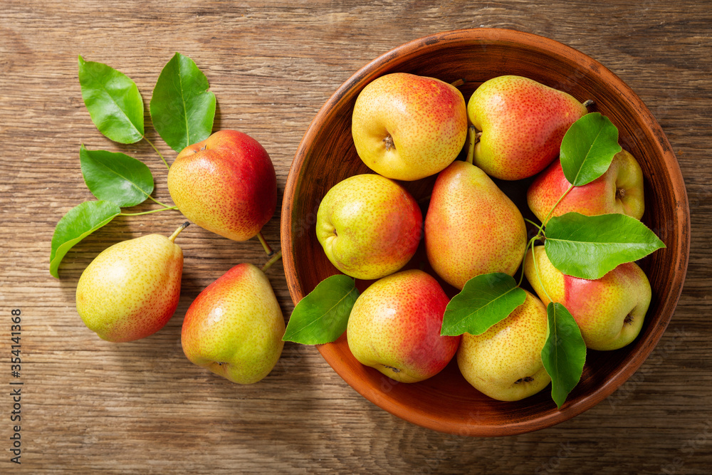 fresh pears with leaves in a bowl on a wooden table, top view fresh pears with leaves in a bowl on a wooden table, top view