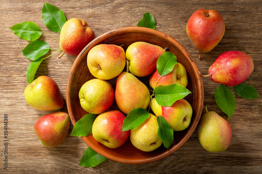 fresh pears with leaves in a bowl on a wooden table, top view fresh pears with leaves in a bowl on a wooden table, top view