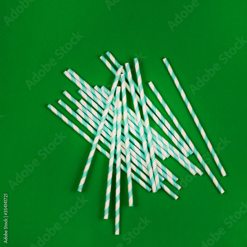 Top view of colorful paper disposable eco-friendly straws. Drinking straw with green stripes for a party on a green background with a copy of the space. The concept of ECO waste.