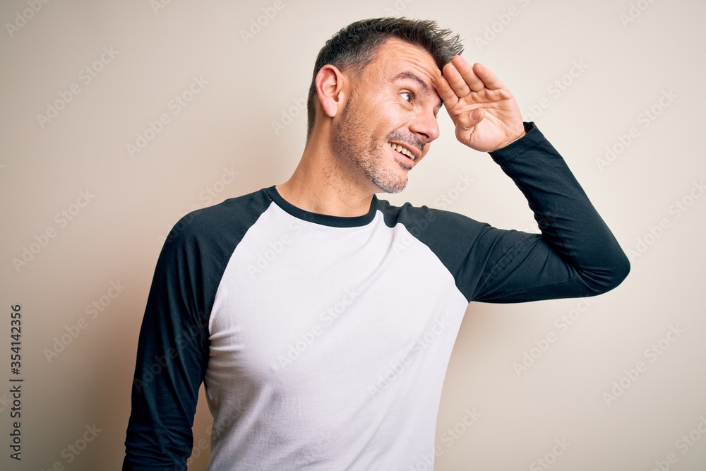 Young handsome man wearing casual t-shirt standing over isolated white background very happy and smiling looking far away with hand over head. Searching concept. Young handsome man wearing casual t-shirt standing over isolated white background very happy and smiling looking far away with hand over head. Searching concept.