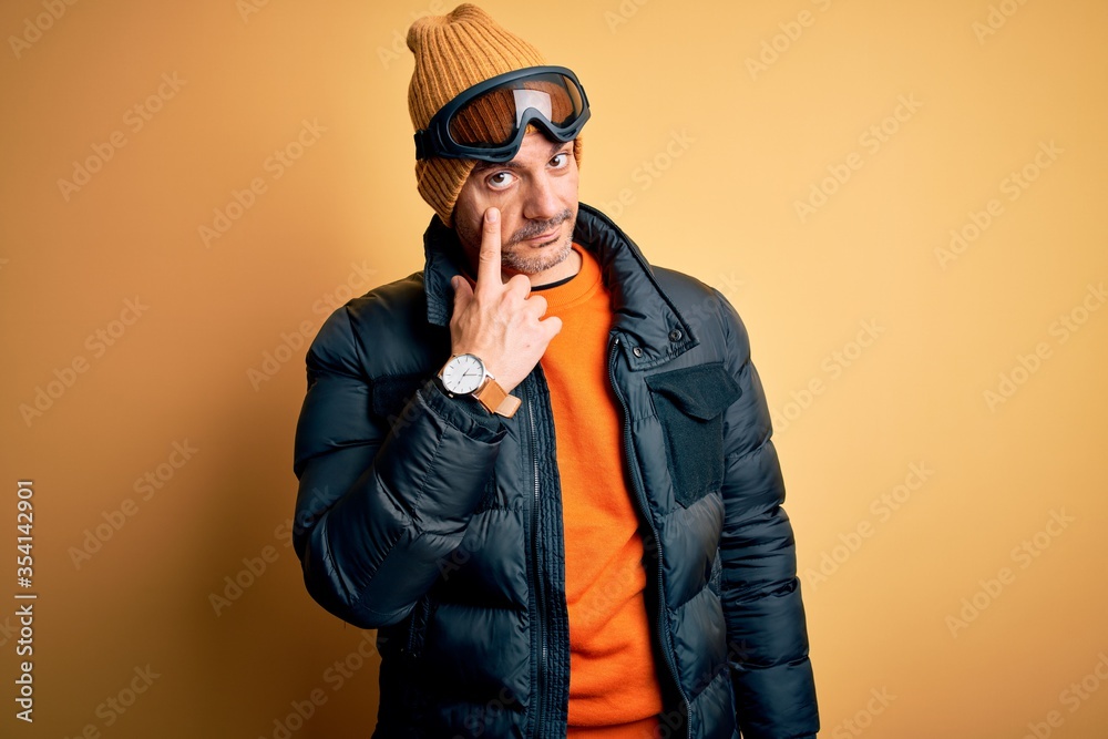 Young handsome skier man skiing wearing snow sportswear using ski goggles Pointing to the eye watching you gesture, suspicious expression Young handsome skier man skiing wearing snow sportswear using ski goggles Pointing to the eye watching you gesture, suspicious expression