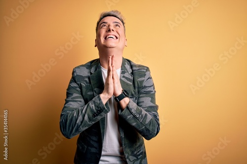 Young handsome modern man wearing business jacket standing over yellow isolated background begging and praying with hands together with hope expression on face very emotional and worried. Begging.