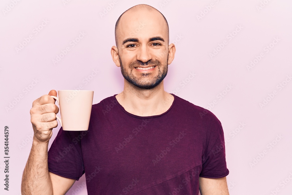 Young handsome bald man drinking cup of coffee looking positive and happy standing and smiling with a confident smile showing teeth Young handsome bald man drinking cup of coffee looking positive and happy standing and smiling with a confident smile showing teeth