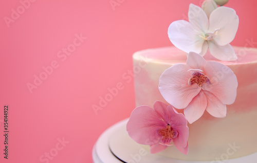 Cake decorated with sugar flowers orchids close-up. Pink marble cake stands on a round white stand on a pink background. Beautiful dessert decorated with flowers.