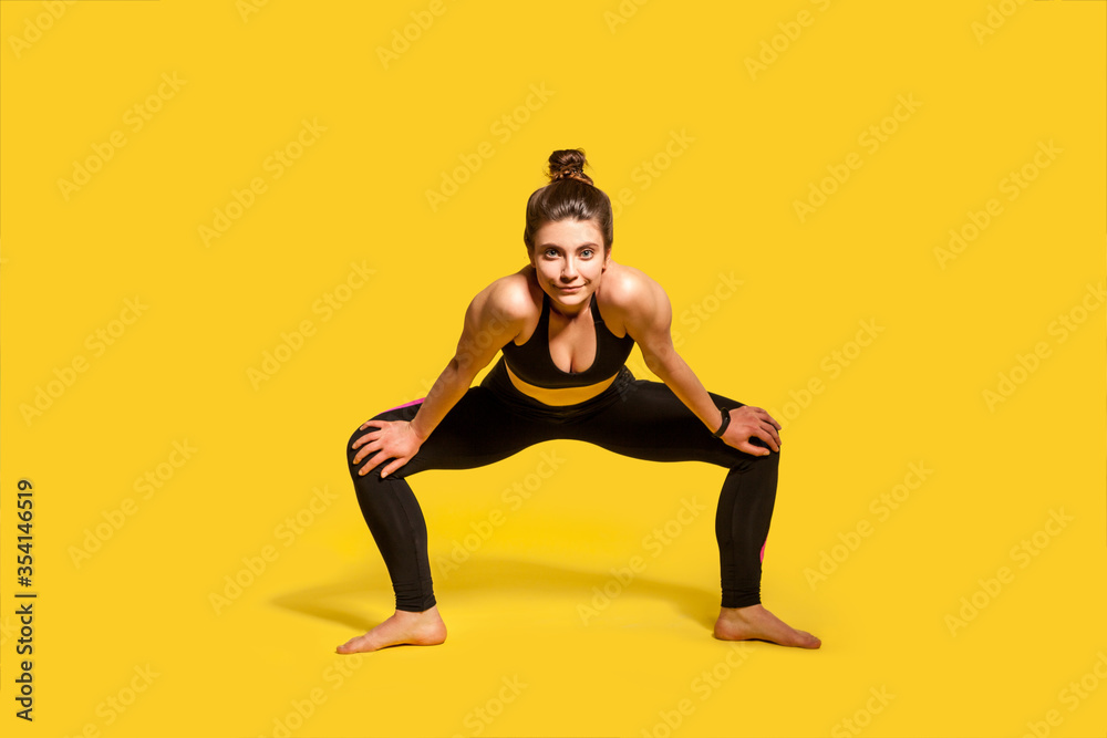 Motivated Assertive Gymnast Girl With Hair Bun In Tight Sportswear Squatting And Spreading Legs