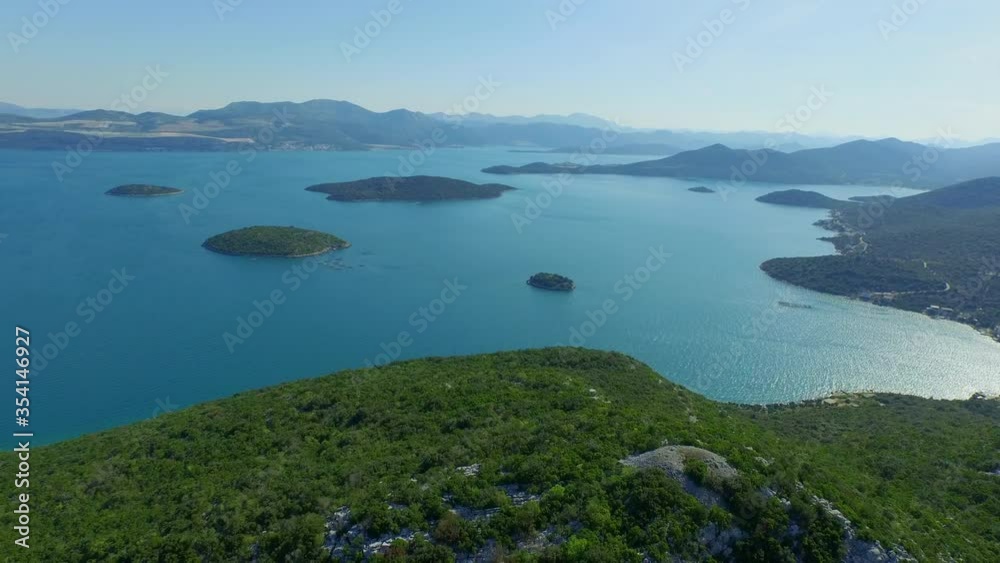 Aerial shot of green mountain by ocean against sky, drone is flying backward - Ston, Croatia Aerial shot of green mountain by ocean against sky, drone is flying backward - Ston, Croatia