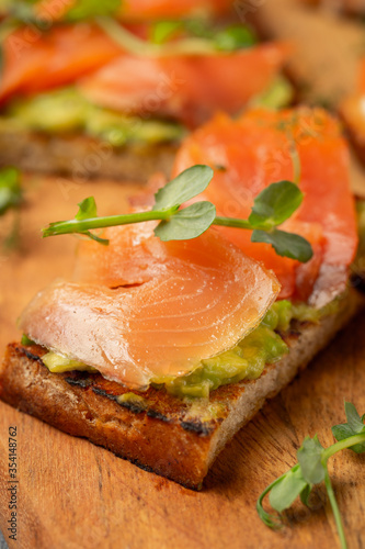 bruschetta with trout or salmon and avocado on a wooden board decorated with microgreens