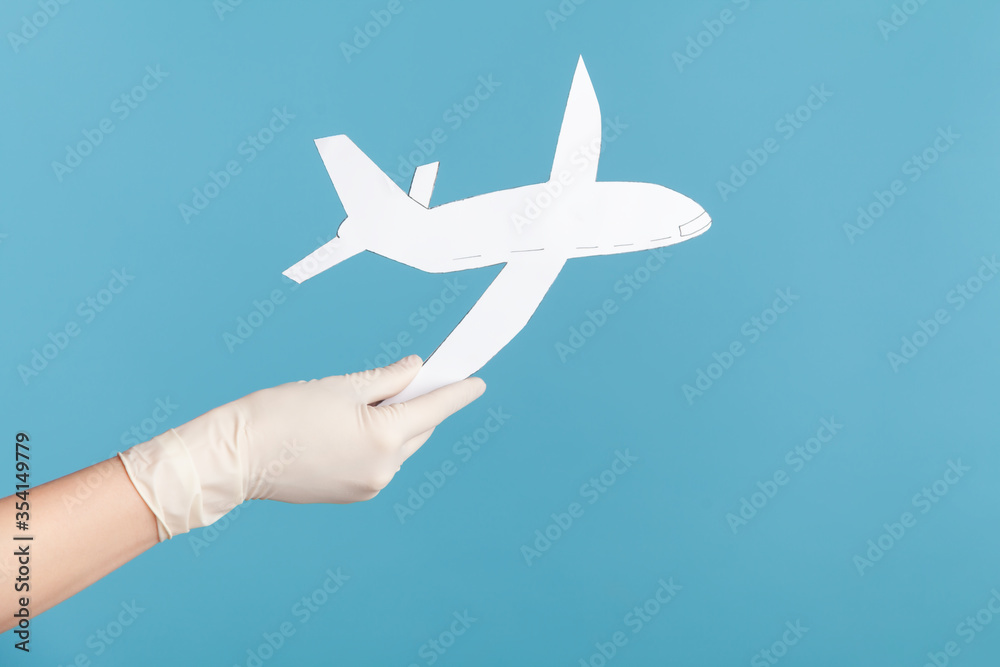 Profile side view closeup of human hand in white surgical gloves holding airplane paper. indoor, studio shot, isolated on blue background. Profile side view closeup of human hand in white surgical gloves holding airplane paper. indoor, studio shot, isolated on blue background.