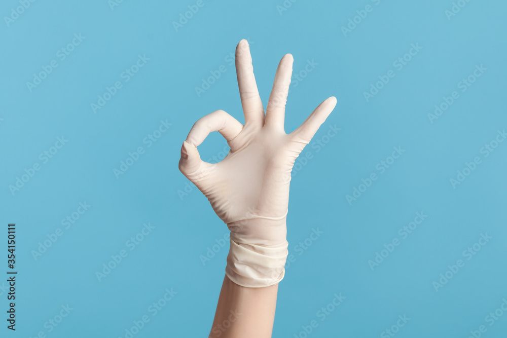 Profile side view closeup of human hand in white surgical gloves showing Ok sign or number 3 with fingers. indoor, studio shot, isolated on blue background. Profile side view closeup of human hand in white surgical gloves showing Ok sign or number 3 with fingers. indoor, studio shot, isolated on blue background.