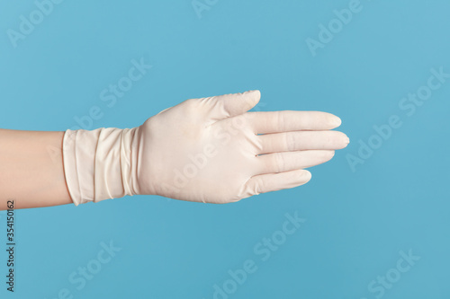 Profile side view closeup of human hand in white surgical gloves giving hand to greeting or touching. indoor, studio shot, isolated on blue background.