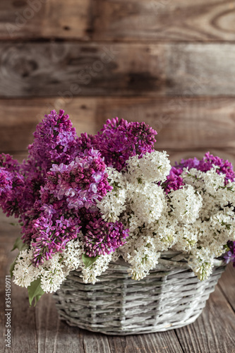 Spring composition lilac flowers in a basket on a wooden background.