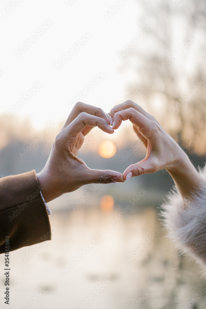 Couples hands are making a heart sign with sun inside Couples hands are making a heart sign with sun inside