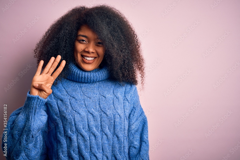 Young beautiful african american woman with afro hair wearing winter sweater over pink background showing and pointing up with fingers number four while smiling confident and happy. Young beautiful african american woman with afro hair wearing winter sweater over pink background showing and pointing up with fingers number four while smiling confident and happy.