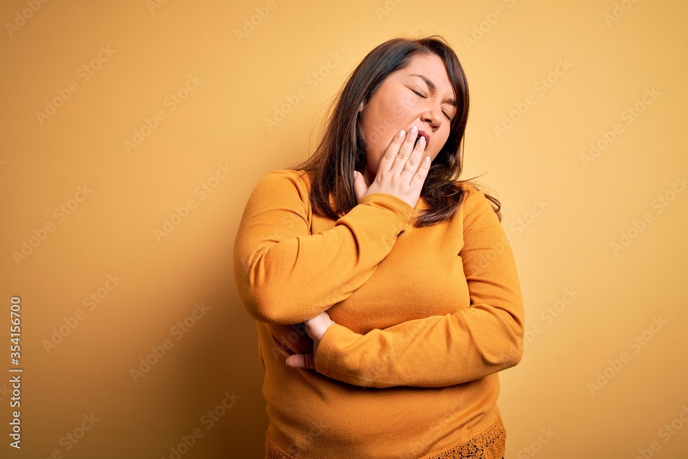 Beautiful brunette plus size woman wearing casual sweater over isolated yellow background bored yawning tired covering mouth with hand. Restless and sleepiness. Beautiful brunette plus size woman wearing casual sweater over isolated yellow background bored yawning tired covering mouth with hand. Restless and sleepiness.