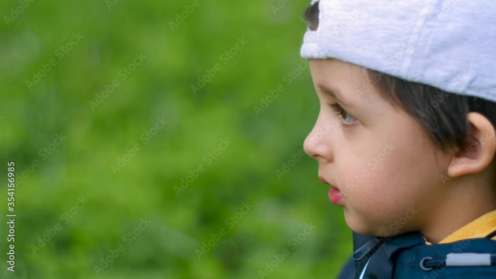 boy in a blue jacket and a gray cap stands on a green field and points ahead and shouts boy in a blue jacket and a gray cap stands on a green field and points ahead and shouts