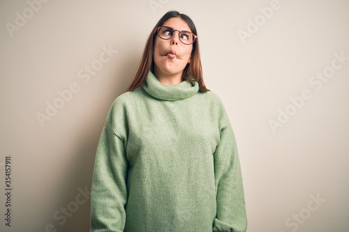 Young beautiful woman wearing casual sweater standing over isolated white background making fish face with lips, crazy and comical gesture. Funny expression. © Krakenimages.com